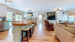 A spacious kitchen with a central island, dining area with a sofa, and a television. - Ocean-view dog-friendly home across street from beach with private pool, W/D, AC (Edisto Beach)