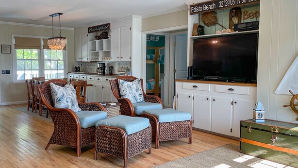 A living room with wicker furniture, a television, and a kitchen area in the background. - Ocean-view dog-friendly home across street from beach with private pool, W/D, AC (Edisto Beach)