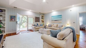 A spacious living room with a high ceiling, a ceiling fan, and a large window with a view of the outdoors. - Natural Wonder (Edisto Beach)