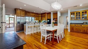 A modern kitchen with wooden cabinets, a central island with chairs, a dining table, and a chandelier. - Natural Wonder (Edisto Beach)