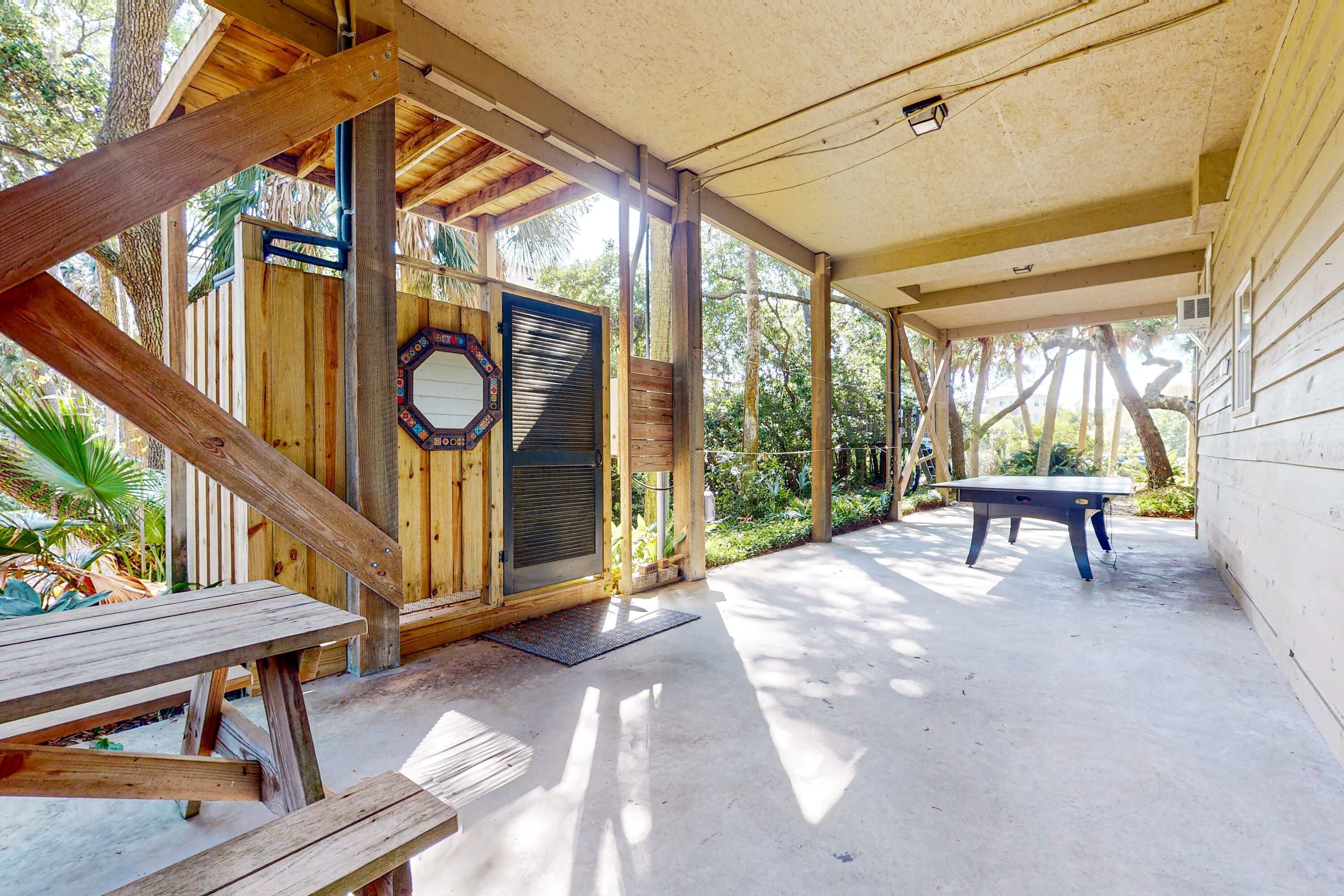 A covered outdoor area with a wooden bench, a table, and a door with a decorative glass panel.