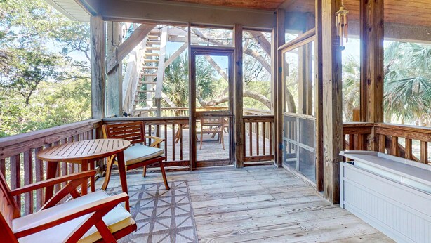 A wooden deck with a table and chairs, a covered area with a view of palm trees. - Natural Wonder (Edisto Beach)