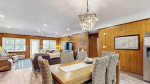Ein Zimmer mit Holzwandverkleidung, einem Esstisch, Stühlen, einer Chandelier und einem Fernseher.