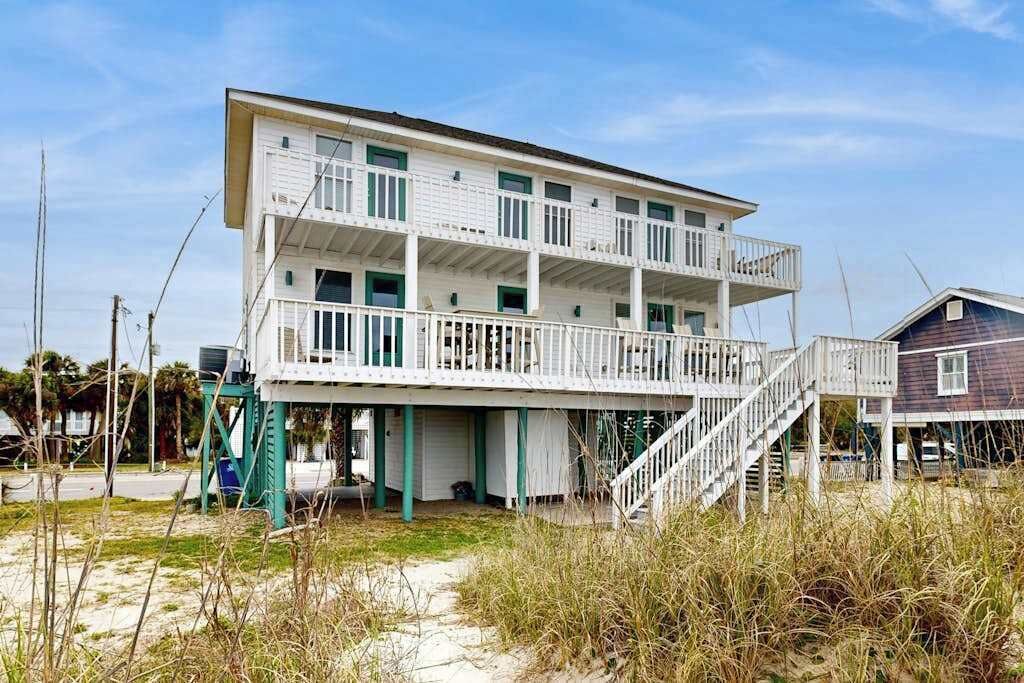 A two-story beachfront house with a balcony, a staircase, and a small porch.