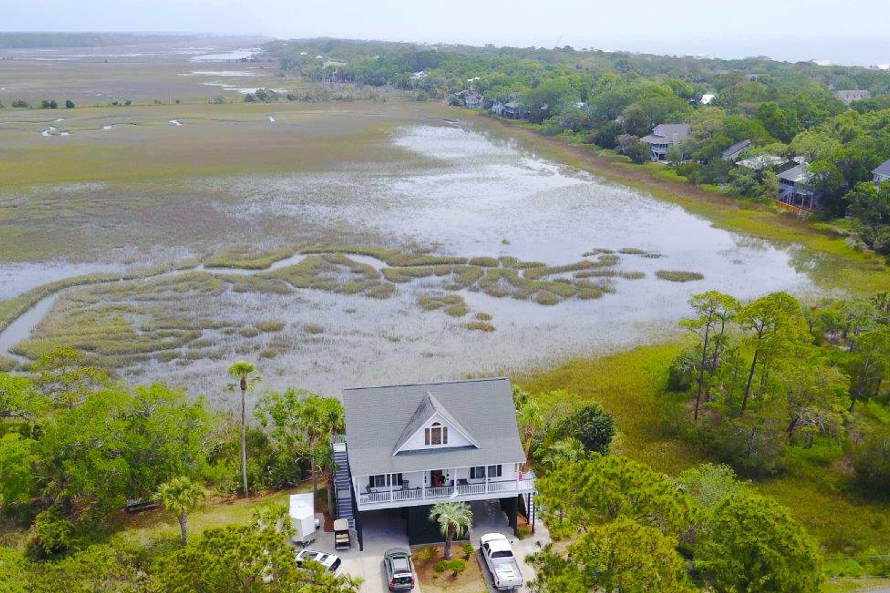 A house with a large front yard, a driveway, and a body of water in the background.