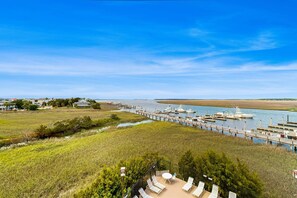 Vista costera con un muelle, barcos y un área verde con sillones de descanso.