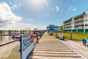 A wooden pier leading to a building with balconies, a sign for 'Edisto Marina', and a view of the water.