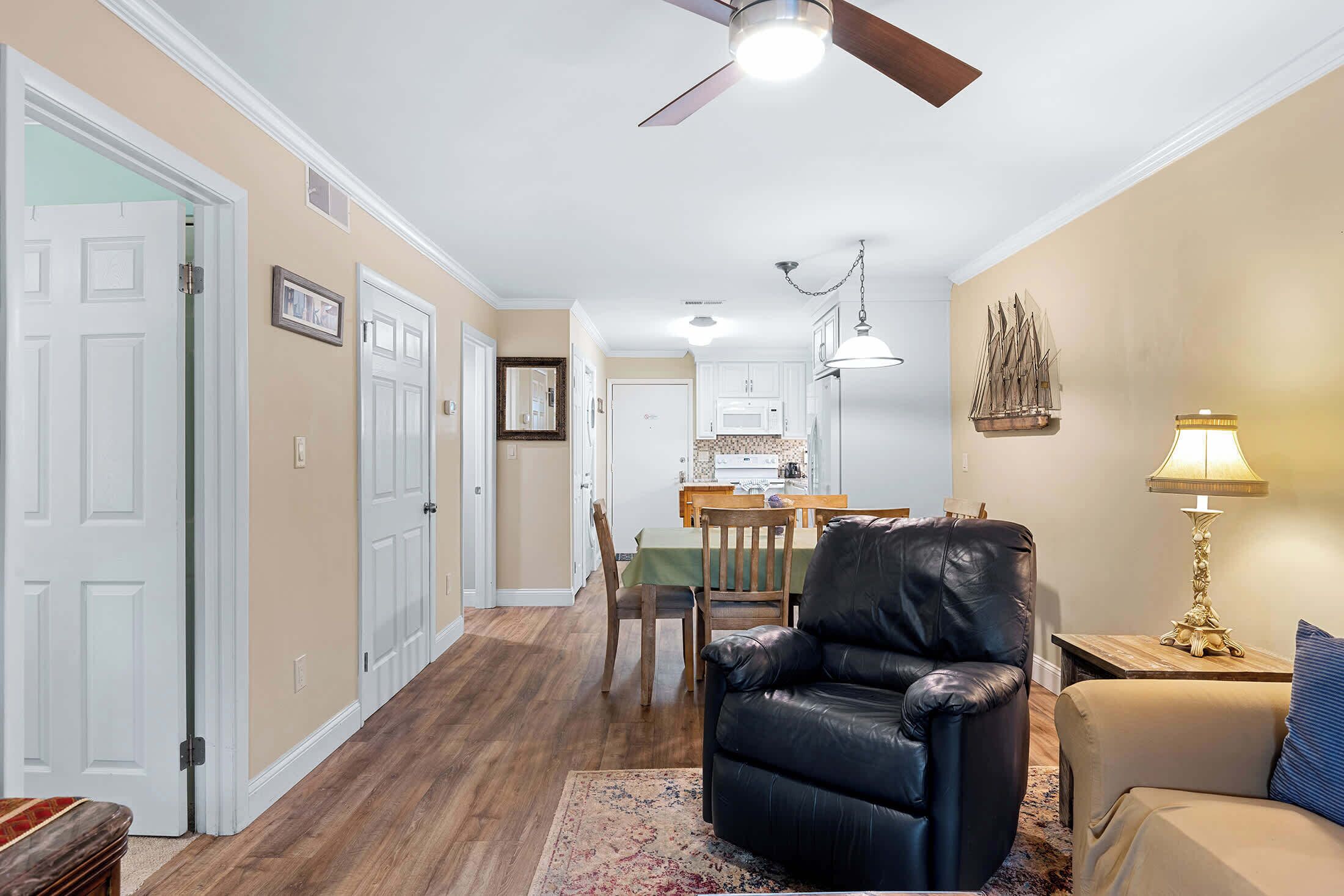 A hallway with a dining area, a black leather chair, a lamp, and a ceiling fan.