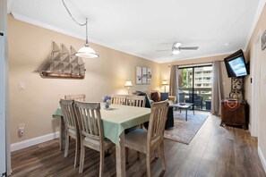 Un comedor con una mesa, sillas, un tapiz con motivos náuticos y un televisor sobre un mueble.