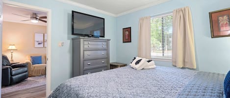 A bedroom with a bed, a dresser, a television, and a ceiling fan.