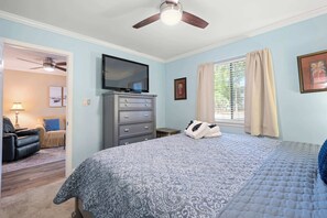 Un dormitorio con cama, cómoda, televisor y ventilador de techo.