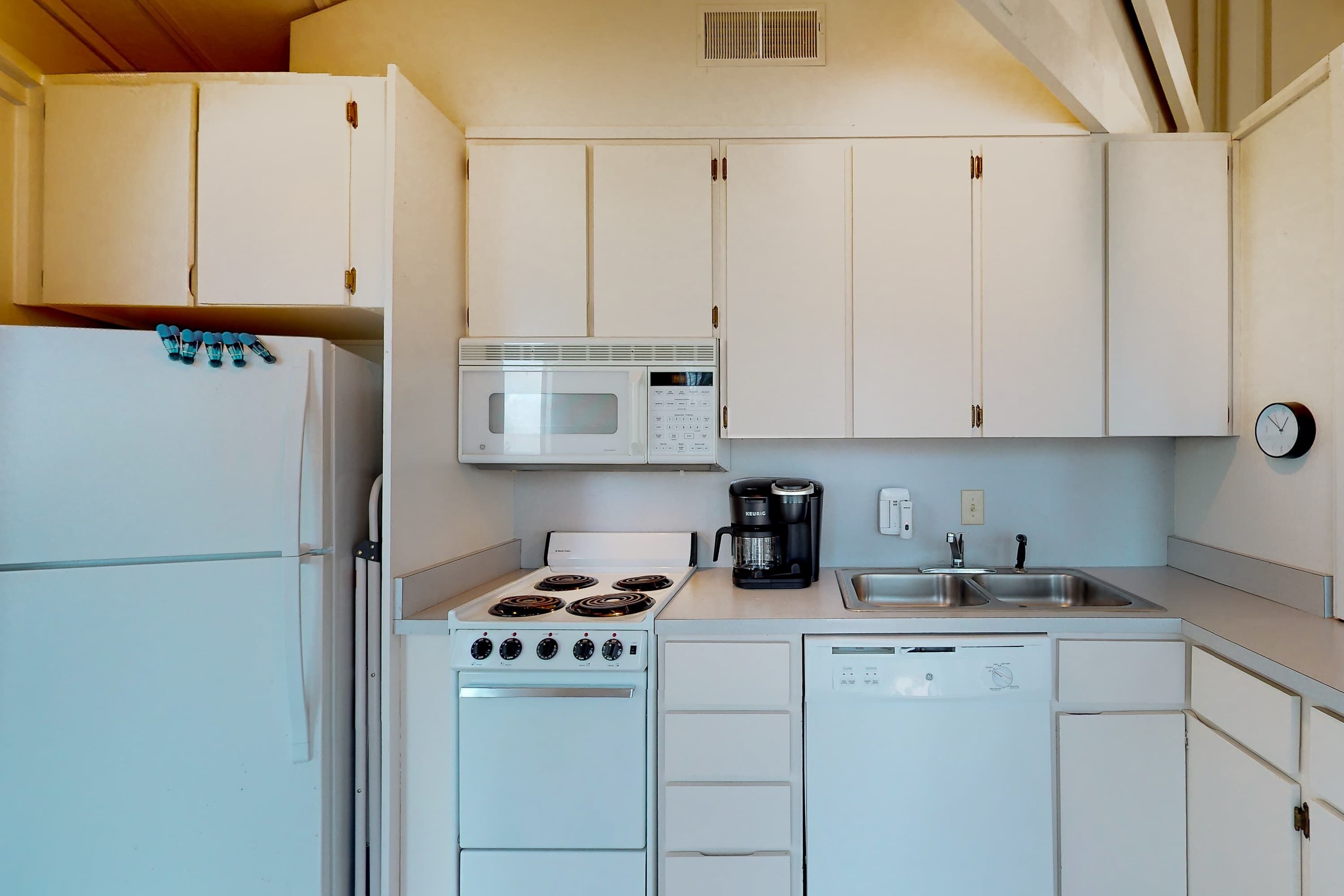 A compact kitchen with white cabinets, a microwave, a stove, a coffee maker, and a dishwasher.