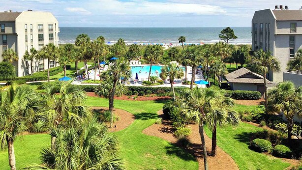 Un resort con piscina, palme e vista sull'oceano.