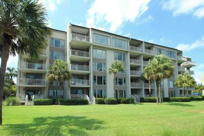 A multi-story hotel with balconies, a grassy lawn, and palm trees. - Updated beach gem with ocean views, pool, hot tub, & tennis - snowbird-friendly (Hilton Head)