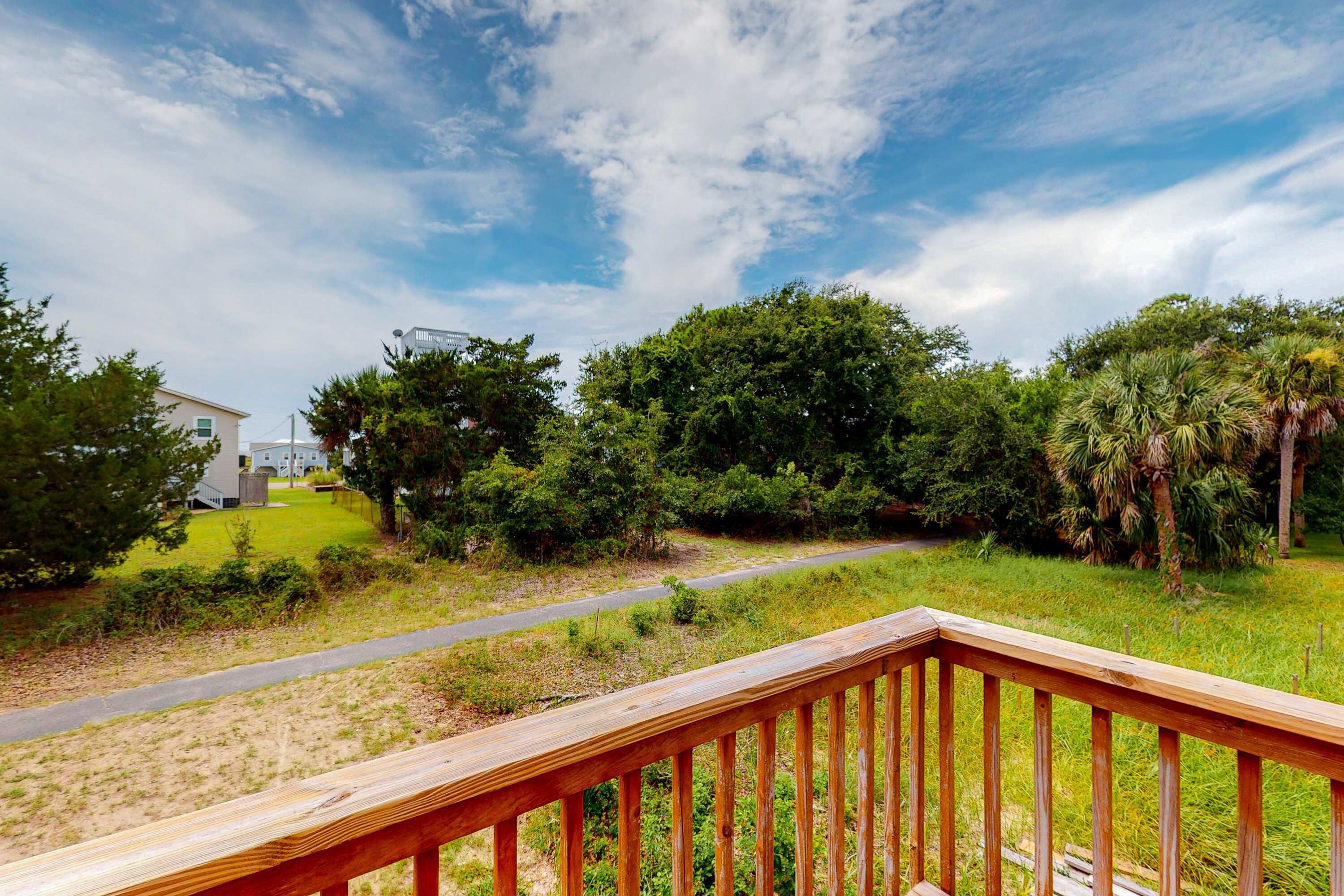 A wooden deck with a grassy area, trees, and a pathway leading to a building.