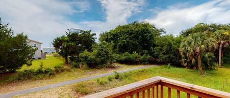 A wooden deck with a grassy area, trees, and a pathway leading to a building.
