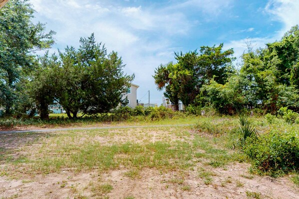 A grassy area with trees and a building in the background. - Recently Updated Home w/Free WiFi, Screened Porch, & A/C (Edisto Beach)