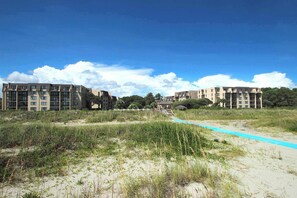 Een strandhotel met meerdere gebouwen, een zandpad en een heldere lucht.