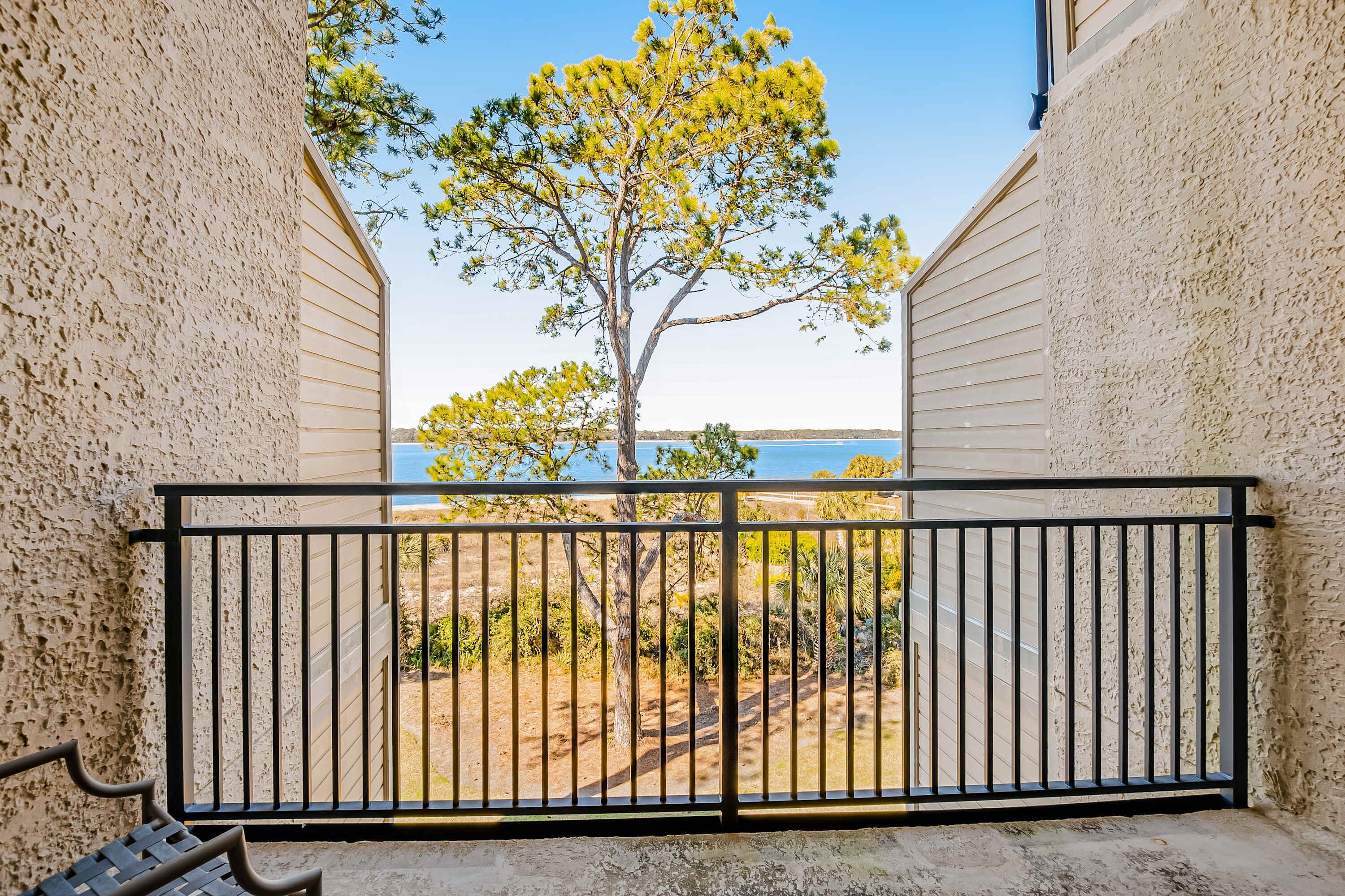 A balcony with a metal railing, a bench, and a view of a tree and landscape.