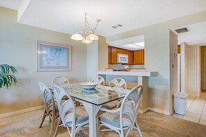 A dining area with a glass-top table, wicker chairs, a chandelier, and a framed picture on the wall. - Beachfront condo with large furnished balcony, pool & beautiful views (Hilton Head)