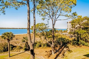 A coastal view with trees, a beach, and a building with multiple floors. - Beachfront condo with large furnished balcony, pool & beautiful views (Hilton Head)