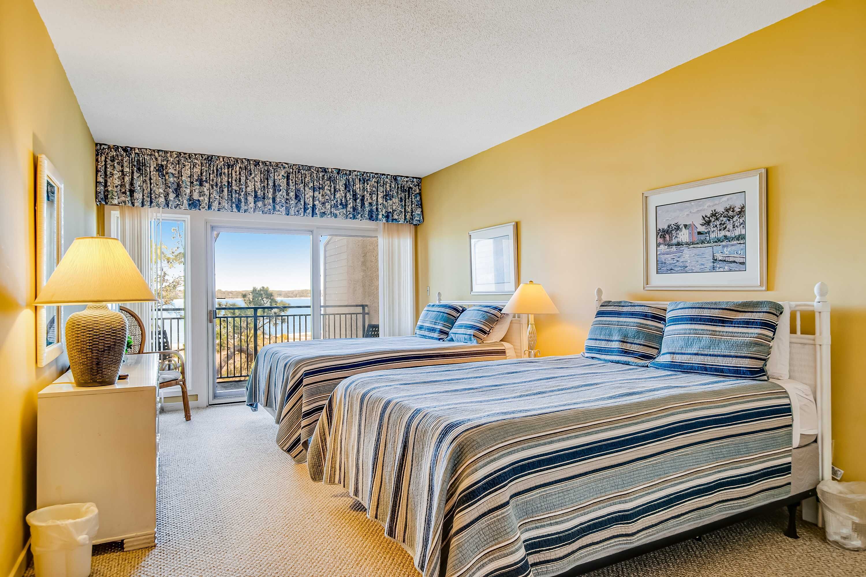 A hotel room with two beds, a balcony, a large window, and a framed picture on the wall.