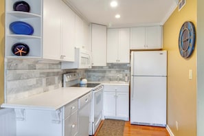 A compact kitchen with white cabinetry, a microwave, a stove, and a refrigerator. - Beachside Condo with Shared Pool & Private Balcony Retreat (Hilton Head)