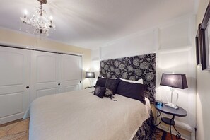 A bedroom with a large bed, a chandelier, two bedside tables with lamps, and a clock. - Spacious condo with shared pool and golf on site Near the ocean (Hilton Head)