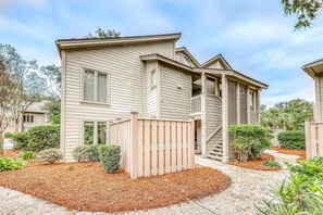A two-story residential building with a front deck, a covered porch, and a small staircase leading to the upper level. - Spacious condo with shared pool and golf on site Near the ocean (Hilton Head)