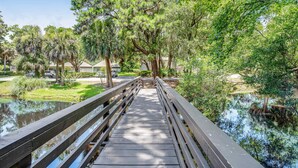 A wooden bridge over a calm body of water, surrounded by lush greenery and trees.