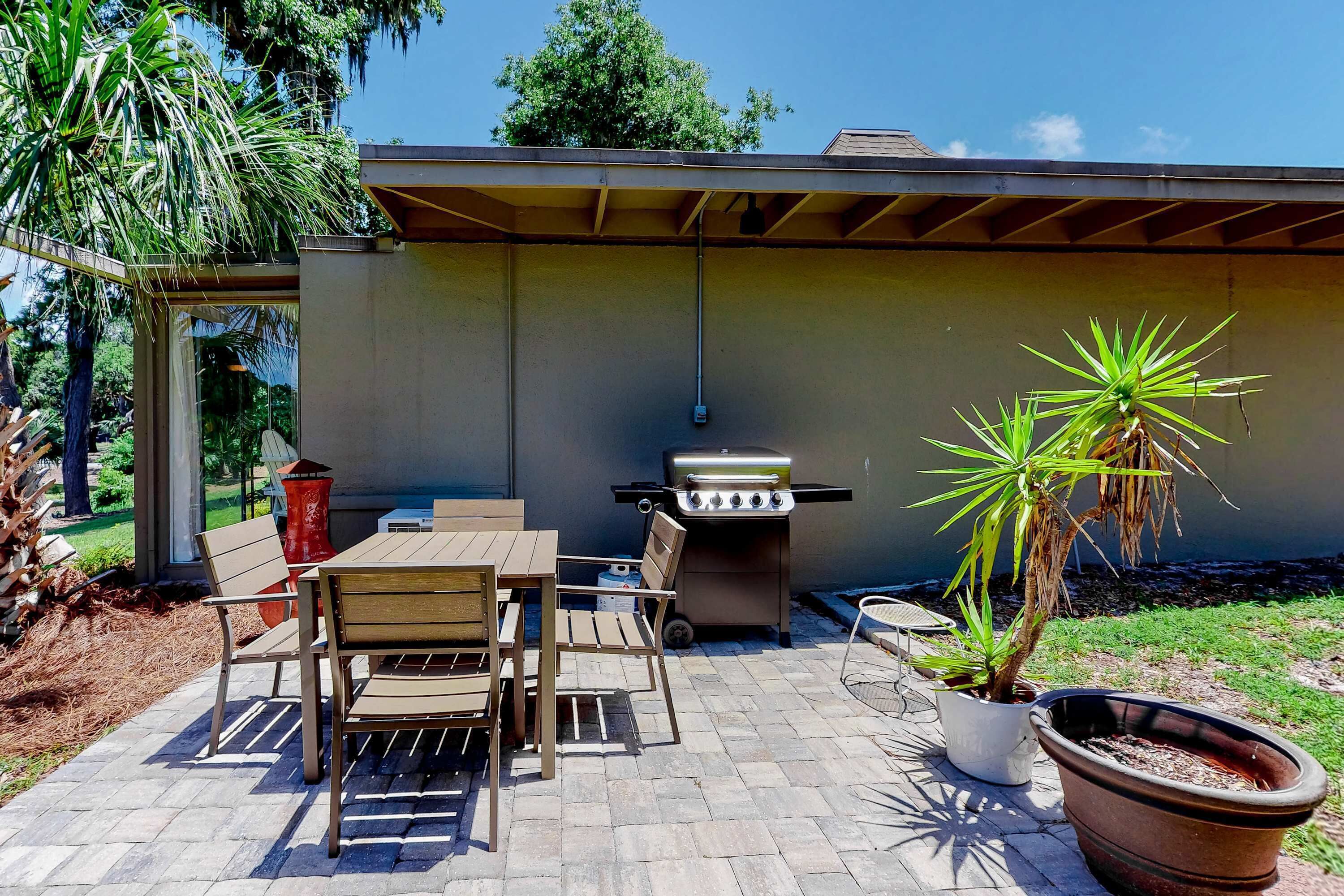 An outdoor patio with a table and chairs, a grill, and potted plants.