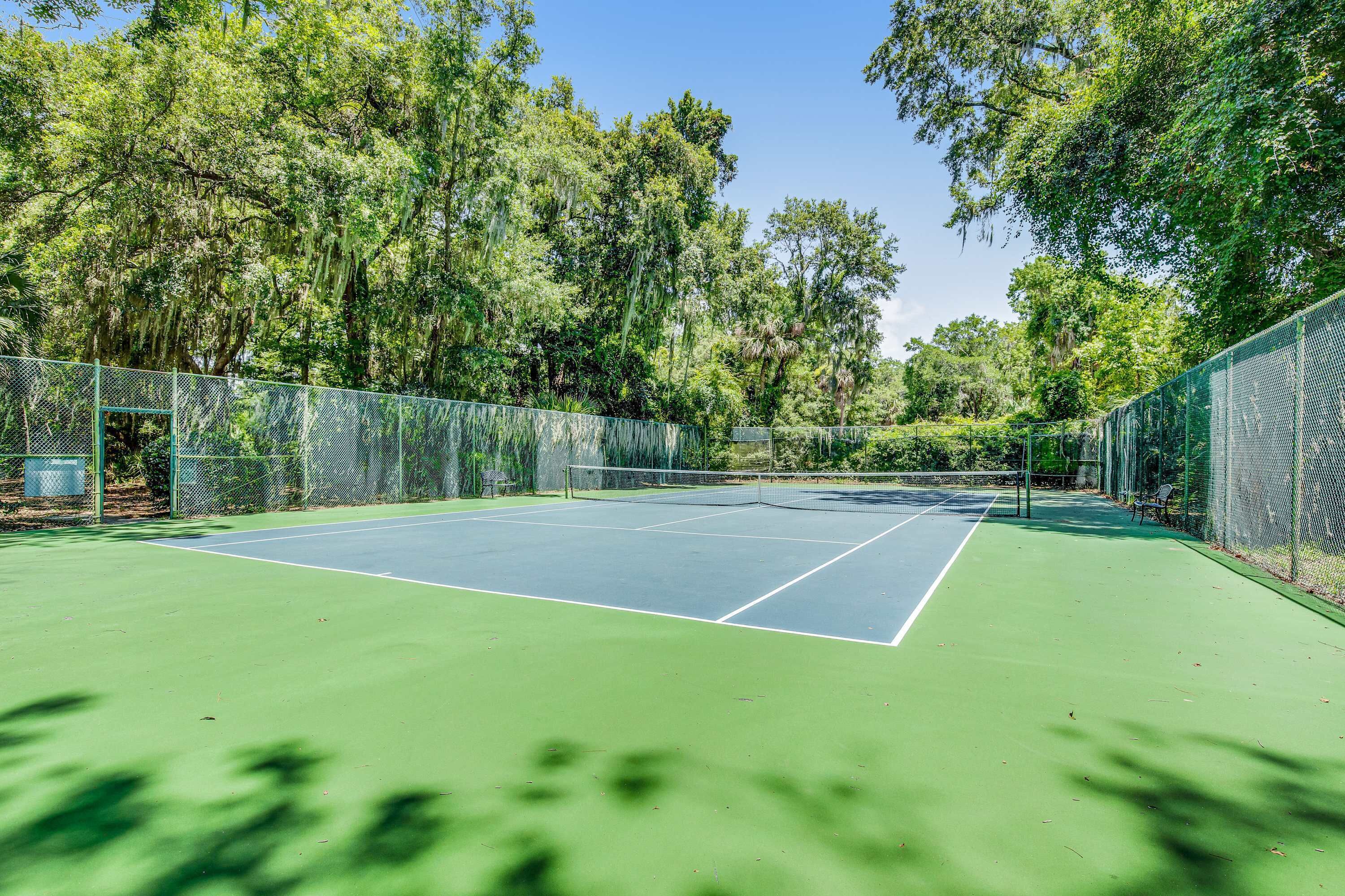 A tennis court surrounded by trees and a green fence.
