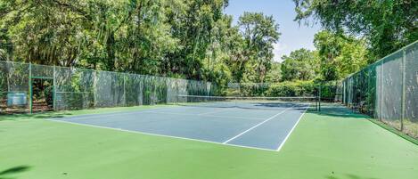 A tennis court surrounded by trees and a green fence.