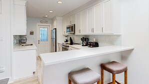 A modern kitchen with white cabinets, a central island, and two bar stools.