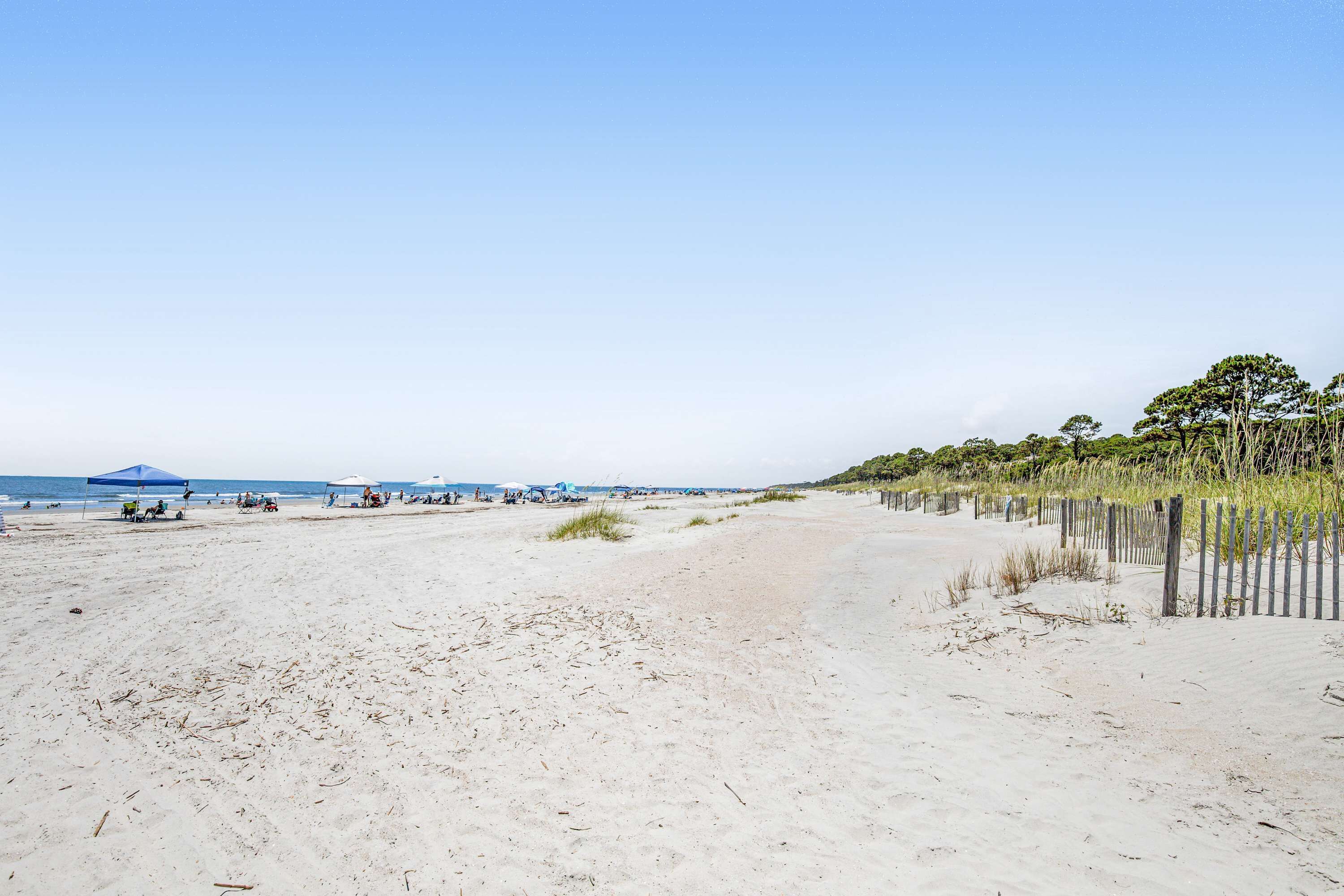 A beach with sand, a fence, and some vegetation.