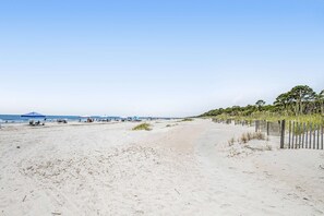 Une plage avec du sable, une clôture et quelques plantes.