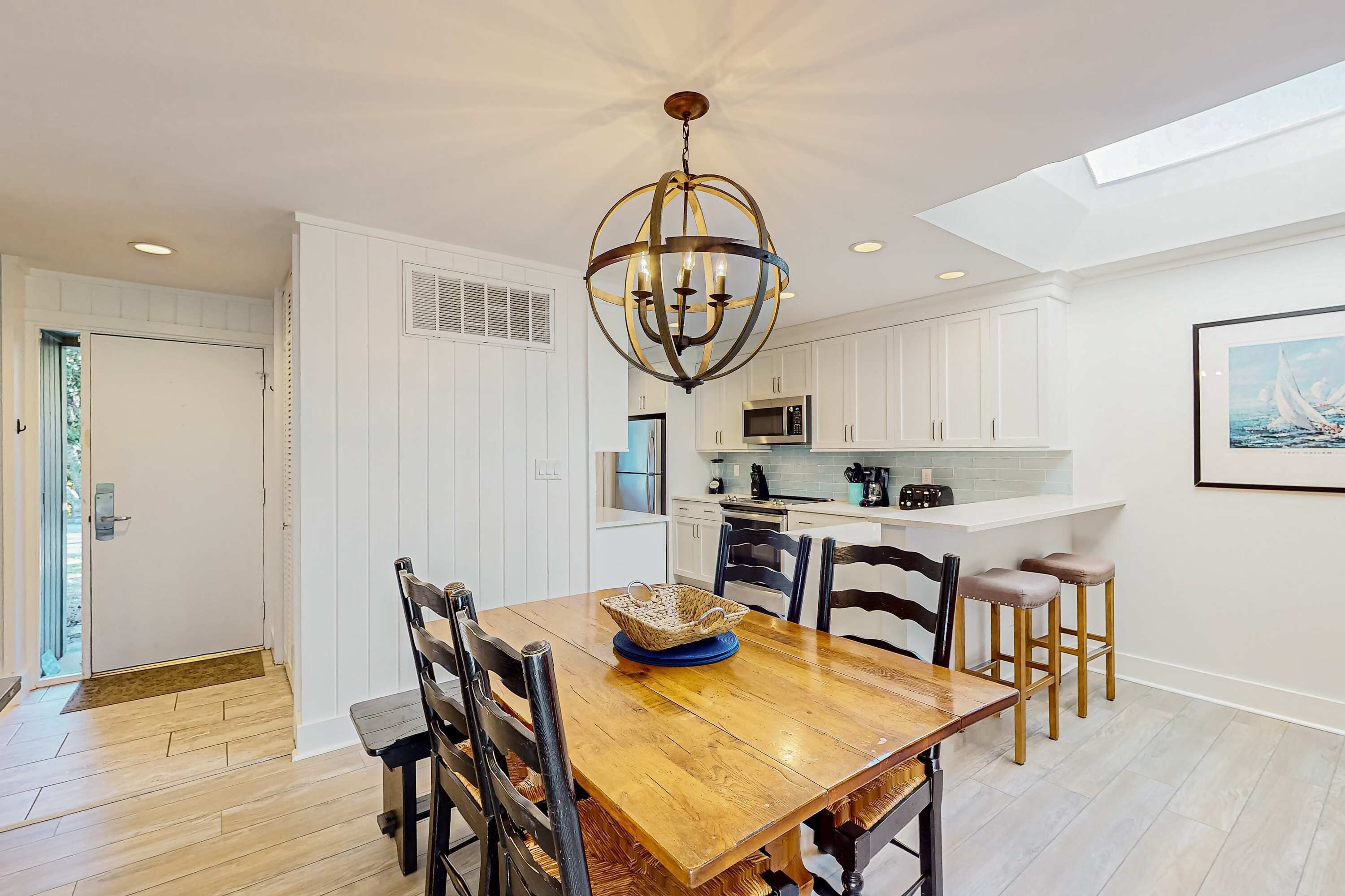 A modern kitchen with white cabinetry, a wooden dining table, and a chandelier.