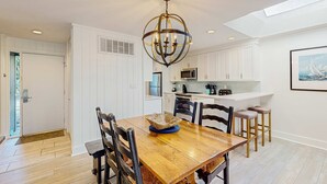 A modern kitchen with white cabinetry, a wooden dining table, and a chandelier.