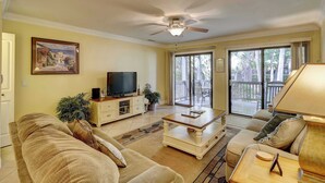 A living room with a sofa, coffee table, TV, and a ceiling fan. - Beautifully remodeled villa with WiFi, inviting porch & balconies walk to beach (Hilton Head)