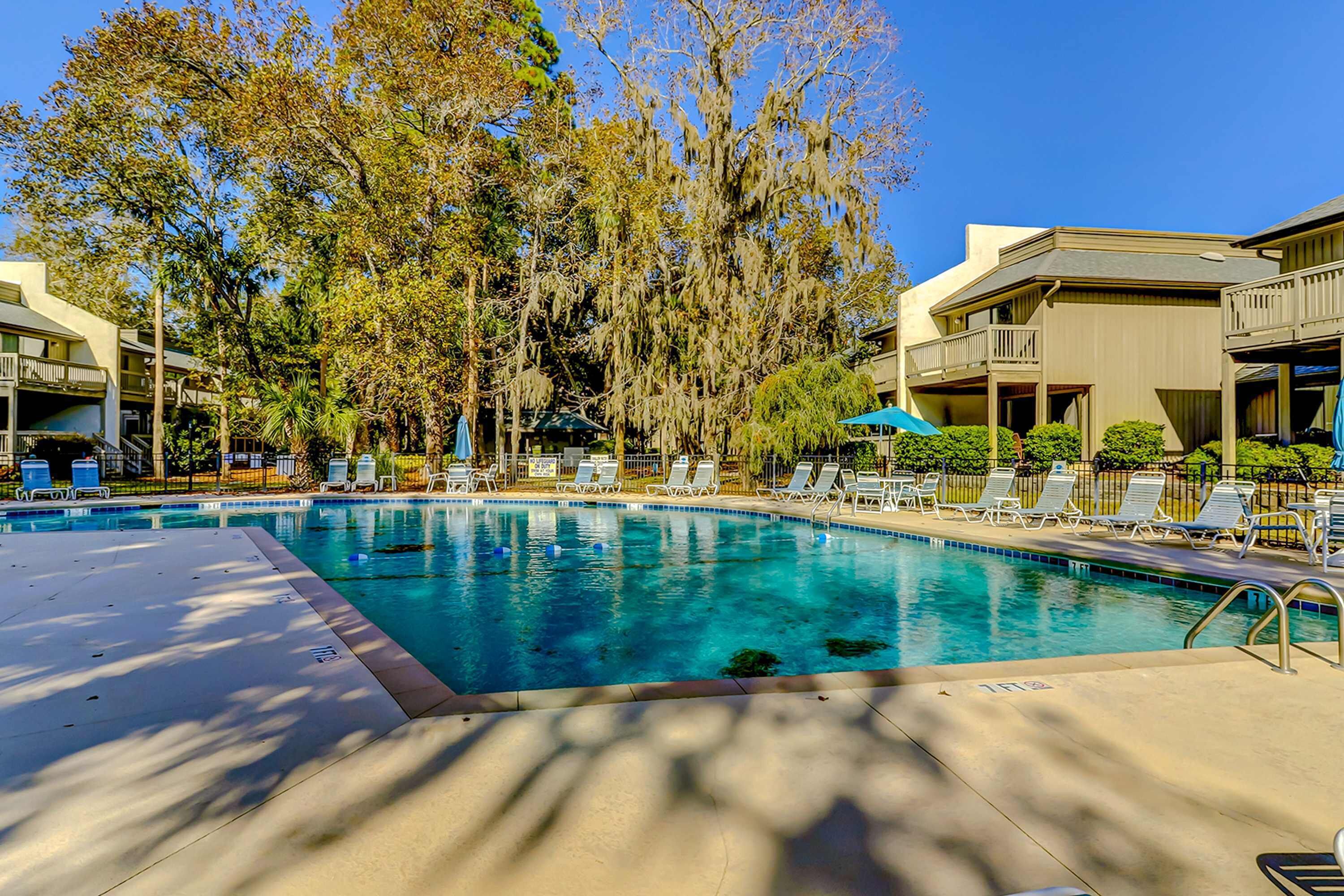 A swimming pool with lounge chairs, surrounded by trees and buildings.