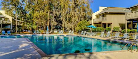 A swimming pool with lounge chairs, surrounded by trees and buildings.