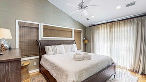 Une chambre avec un grand lit, un ventilateur de plafond et une fenêtre avec des rideaux.