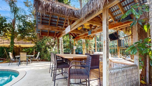 Une terrasse en bois avec une piscine, du mobilier d’extérieur et une structure surmontée d’un toit de chaume.