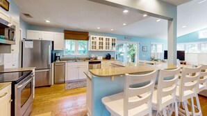 Une cuisine moderne avec des meubles blancs, des appareils en acier inoxydable et un îlot central doté de tabourets de bar.