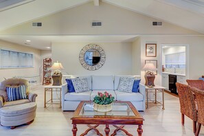 Un salon spacieux avec un canapé blanc, une table basse en verre, un fauteuil en cuir et un coin repas avec des chaises en osier.