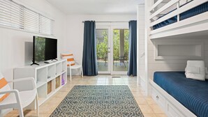 Quarto compacto com cama, televisão, escrivaninha e cadeira.