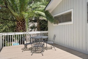 A covered outdoor patio with a table and chairs, a white railing, and a palm tree. - North Forest Beach home with large deck, three houses from the beach (Hilton Head)
