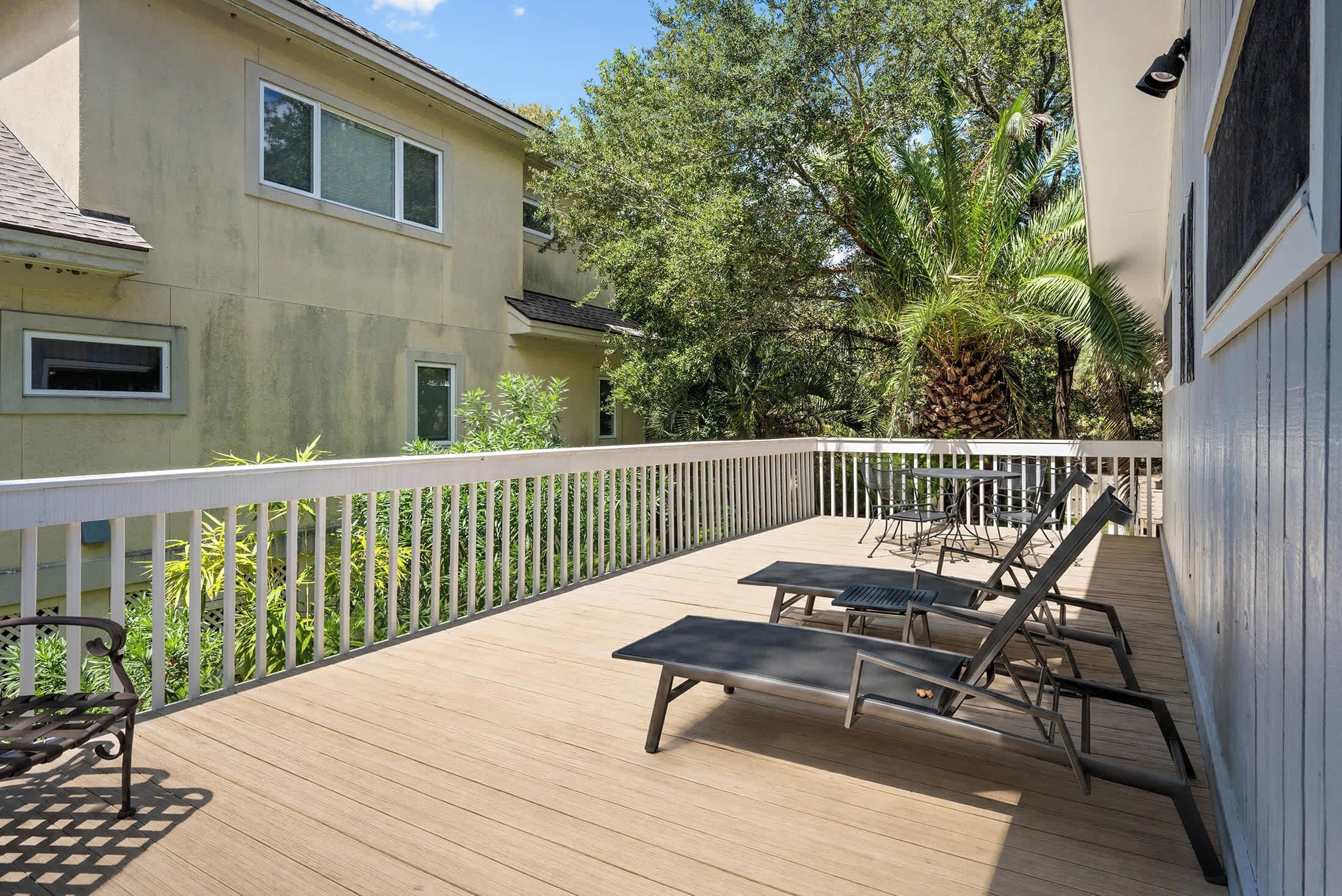 A wooden deck with two lounge chairs and a table, surrounded by a white railing.