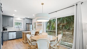 A modern kitchen with grey cabinets, a central island with chairs, and a large window with a view of greenery. - Scenic Golf Front Condo with Large Deck, Resort Pool & Easy Beach Access (Hilton Head)