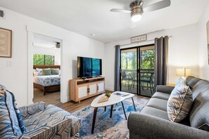 A modern living room with a sofa, a coffee table, a TV, and a dining area with a table and chairs. - Family-friendly condo with top-floor balcony, complex pools, tennis, pickleball (Hilton Head)